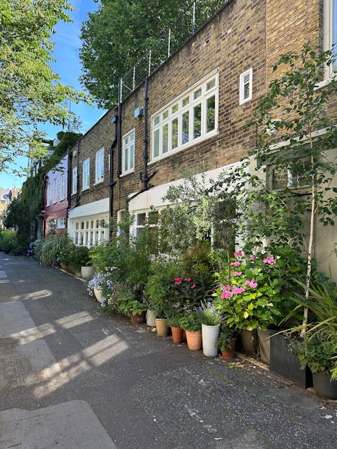 A row of residential buildings along Streatham High Road featuring a variety of potted plants and flowering shrubs in different sizes and colors, including pink, purple, and white blossoms, arranged a